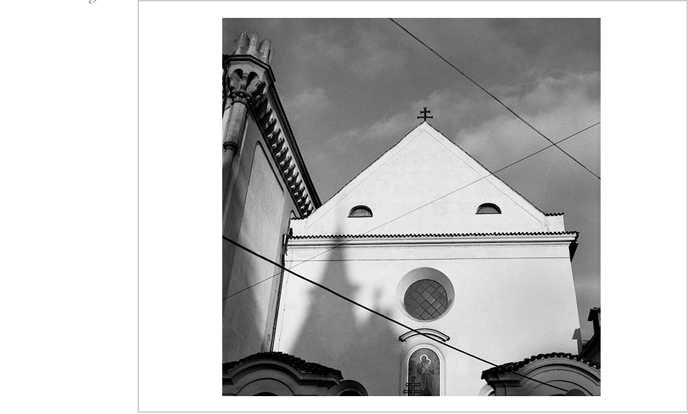 The interplay of power lines and the shawdow of a cathedral frame the facade of a church in historic Prague.
