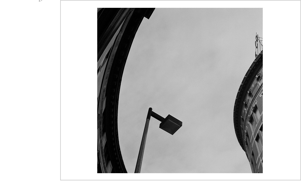 A very square street lamp interrupts the circular arch and the building it mimics.