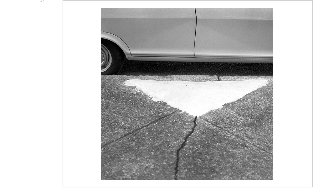 The details of a vintage sedan mesh with those of the street it's parked upon.
