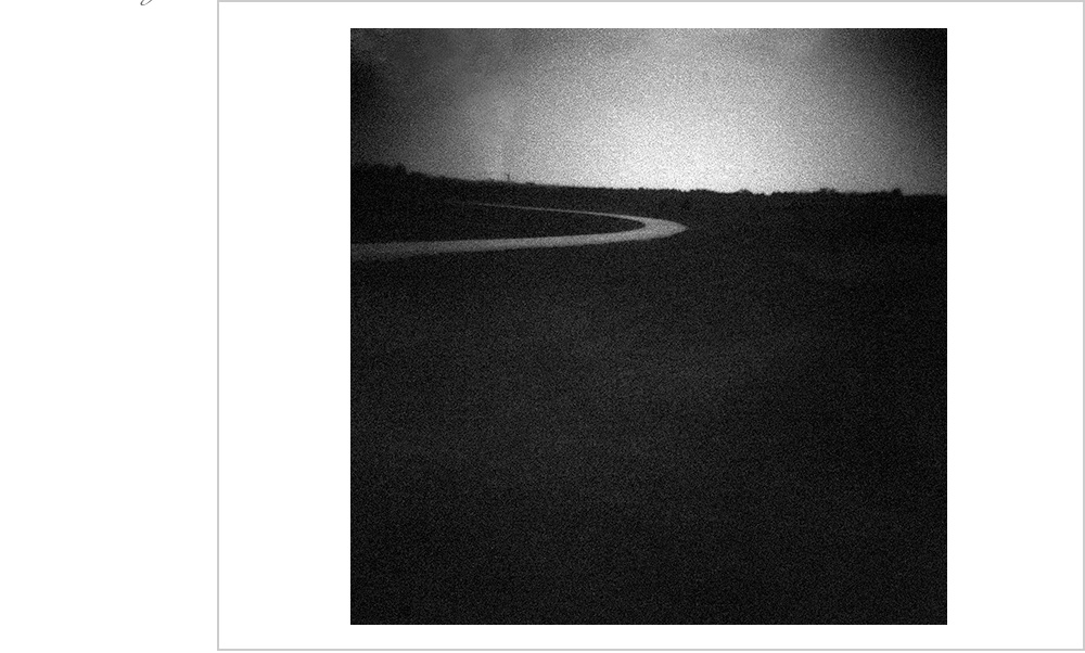 The long slow bend of this old road glows in the dusk night of an Iowa landscape.
