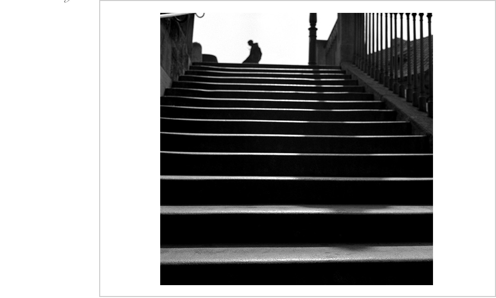 The shadow of a lamp,backlit cascades down the steps of the Charles Bridge in Prague. The silhouette of a figure confounds the mind
