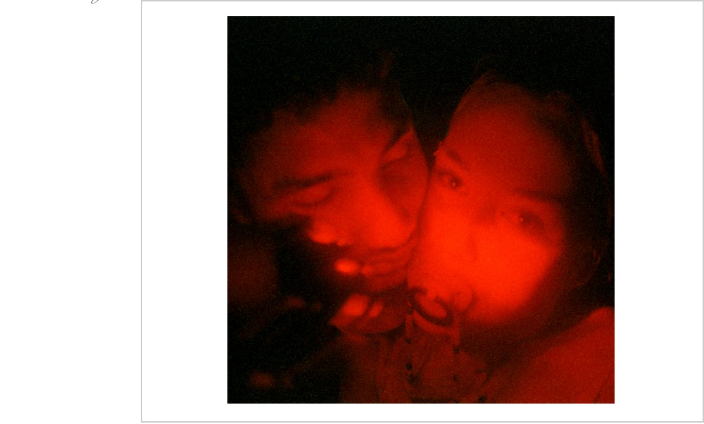 Two young dancers come together in the romantic red glow of glowsticks at an underground rave in Oakland, California in 1999.